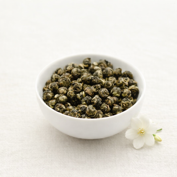 Mrs Oldbucks Pantry Buddhas Tearsjasmine white tea pearls in a white ceramic bowl with a jasmine flower on neutral linen in soft natural light.