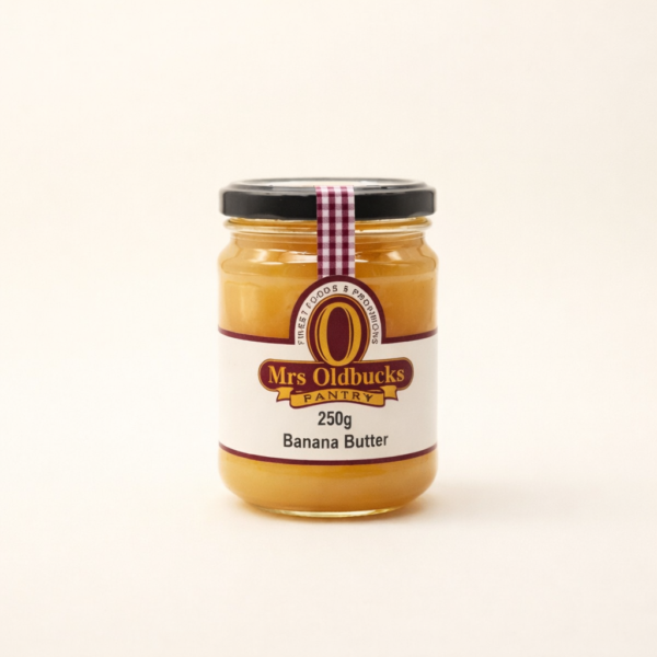 Mrs Oldbucks Pantry Banana Butter250g jar of Mrs Oldbucks Pantry Banana Butter on a warm ivory background, showing smooth golden banana butter in a clear glass jar with black lid and burgundy label.