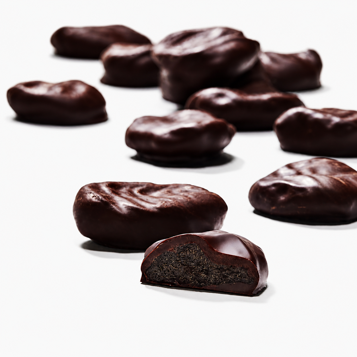 Mrs Oldbucks Pantry Dark Chocolate Brandy Prunes Dark chocolate-coated brandy prunes with a rich glossy couverture chocolate finish, featuring a cut-open piece revealing the soft fruit centre on a clean white background.