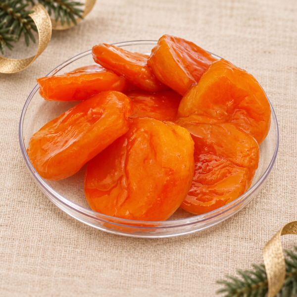 Golden glacé apricots on a clear dish with beige linen, evergreen foliage and gold Christmas ribbon.
