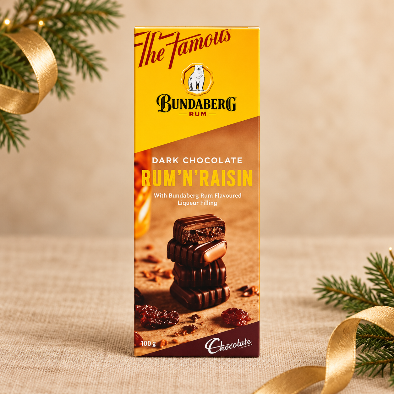 Bundaberg Rum ānā Raisin Dark Chocolate 100g box on beige linen with evergreen foliage and gold Christmas ribbon.
