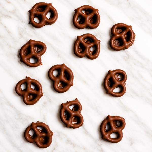 Mrs Oldbucks Pantry Milk Chocolate Milk chocolate coated pretzels arranged on a soft white marble background in an elegant flat-lay confectionery style for Mrs Oldbucks Pantry Pretzels